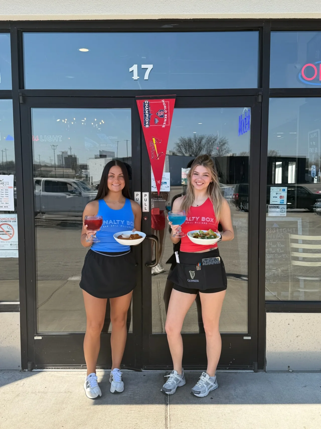 Two Penalty Box servers at the front door of 17 Eastgate Plaza holding fishbowl cocktails, a Bavarian pretzel and a taco salad