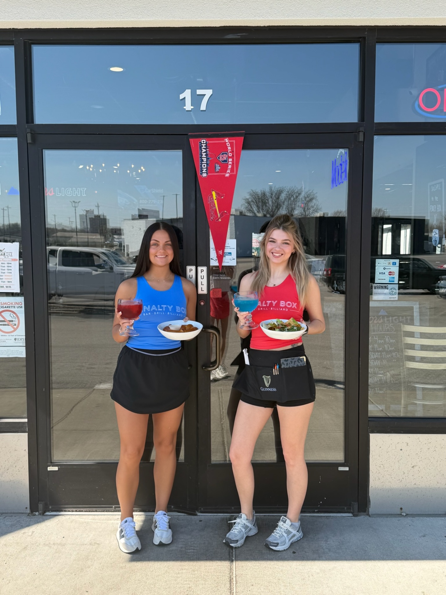 Two Penalty Box servers at the front door of 17 Eastgate Plaza holding fishbowl cocktails, a Bavarian pretzel and a taco salad