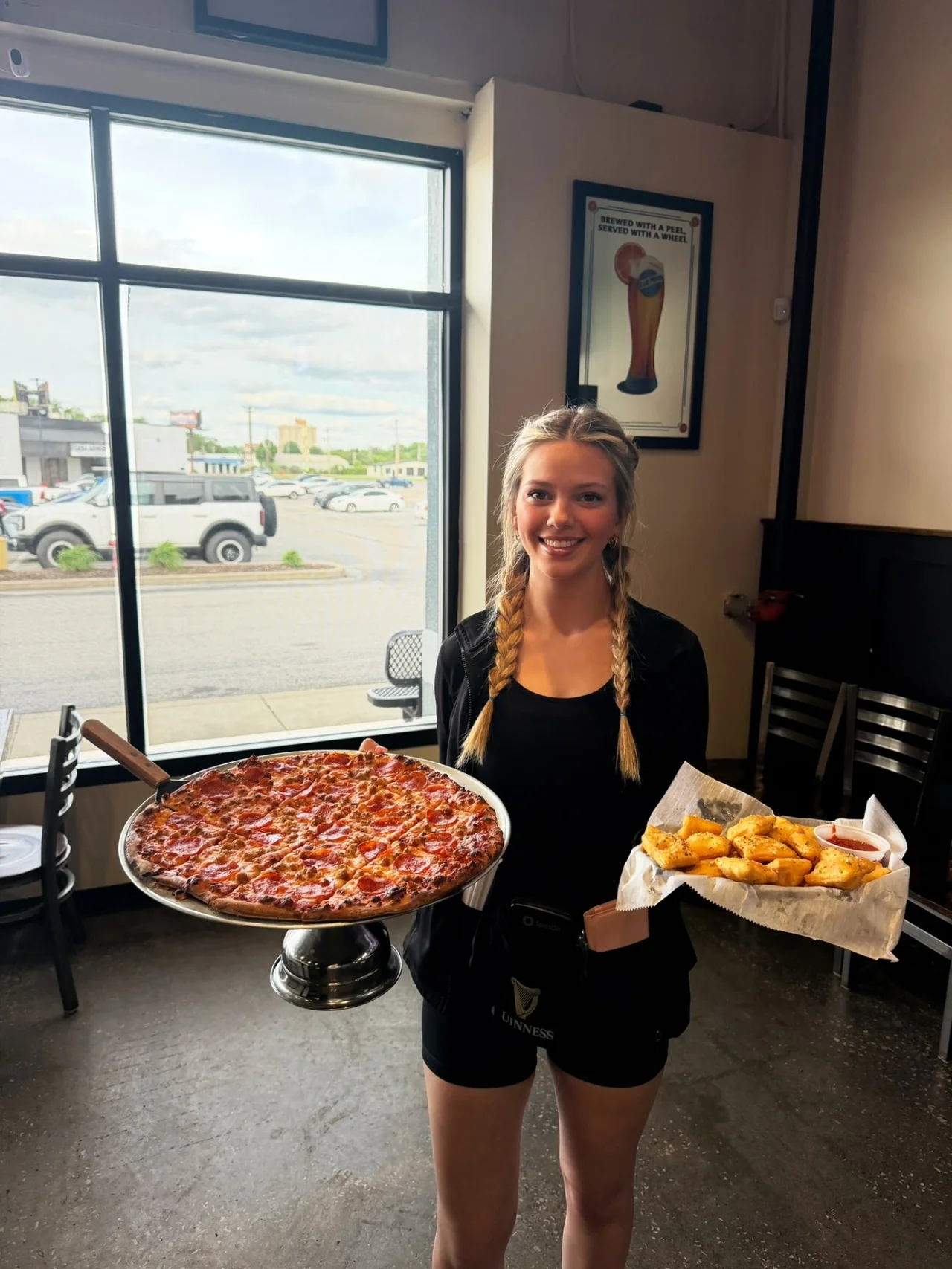 Penalty Box server holding a full pepperoni and sausage pizza on a stand alongside toasted ravioli