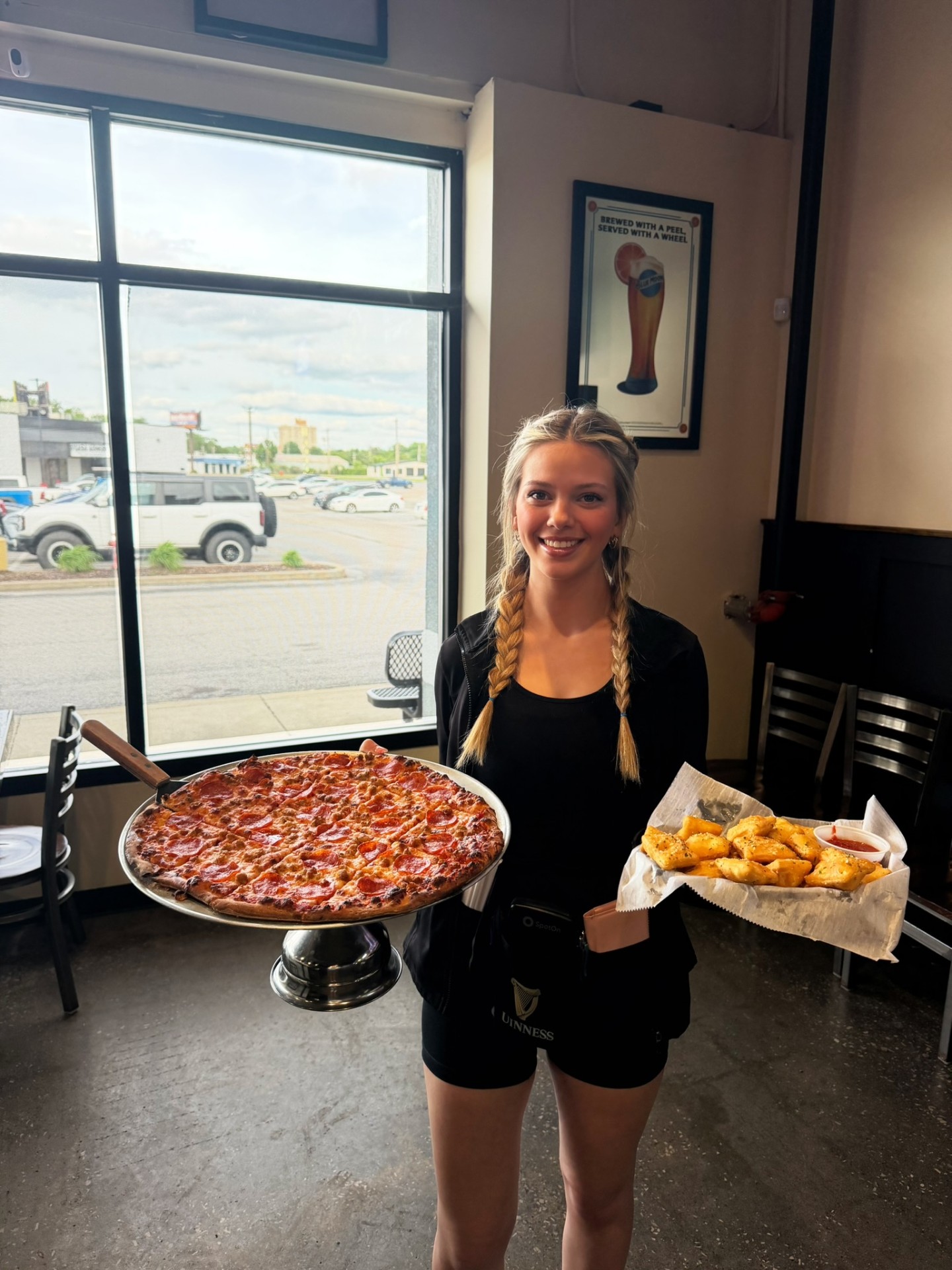 Penalty Box server holding a full pepperoni and sausage pizza on a stand alongside toasted ravioli