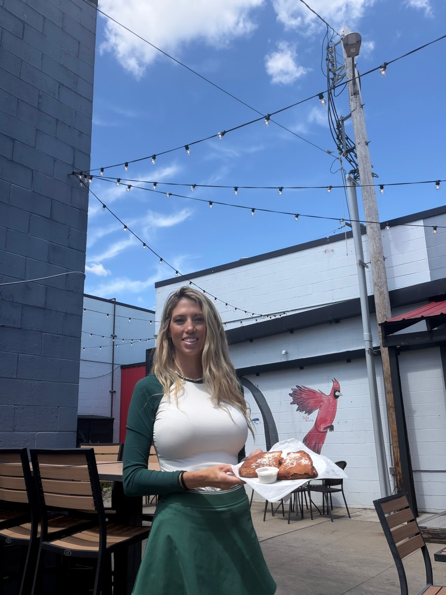 Penalty Box server on the patio under string lights with a jumbo Bavarian pretzel, cardinal mural in the background