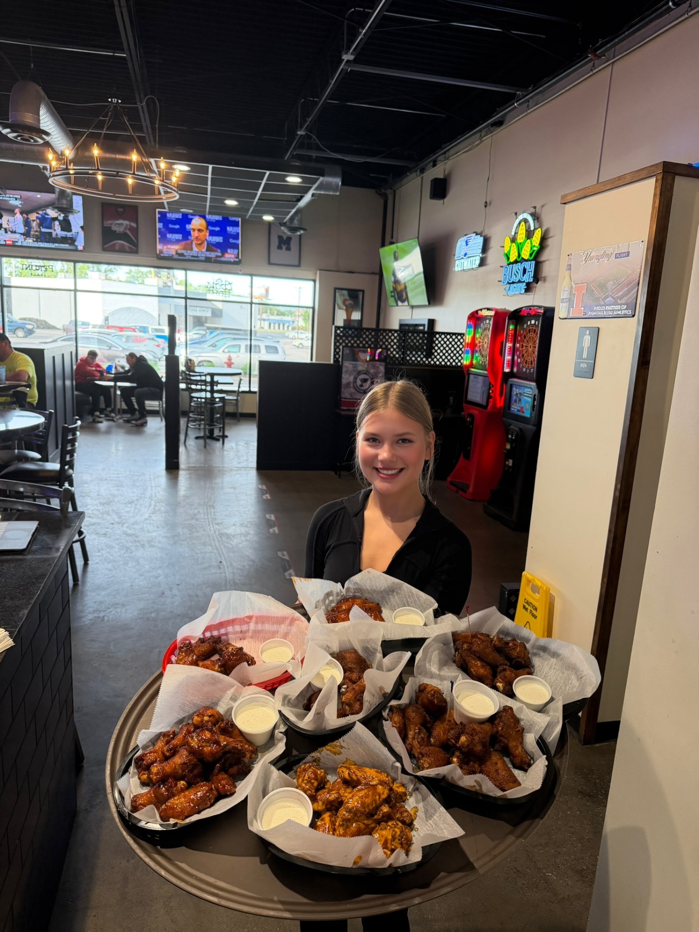 Penalty Box server carrying a tray loaded with six baskets of jumbo wings tossed in BBQ, buffalo, garlic parmesan and dry-rub sauces with ranch dipping cups